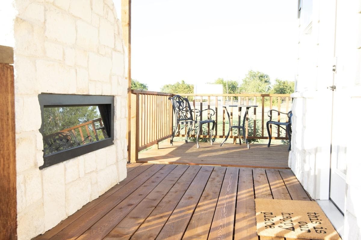 Front porch and deck with a fireplace, table and chairs and a grill.